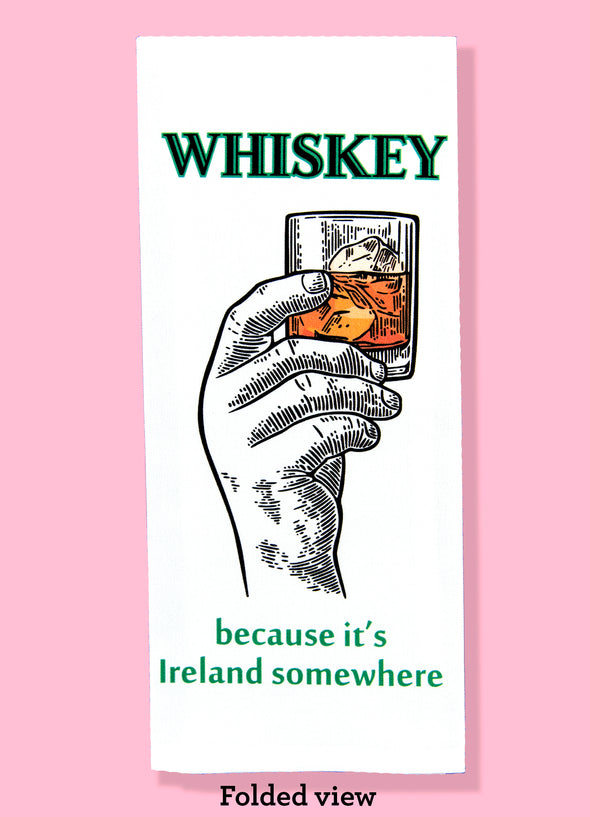 Folded dishtowel with the phrase whiskey because it's Ireland somewhere. The illustration features a hand holding up a half full glass of whiskey and ice