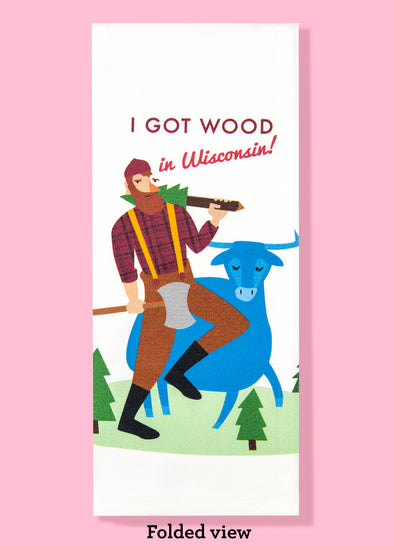 Folded dishtowel with the phrase I got wood in Wisconsin in red with an illustration of a cartoon Paul Bunyan and Babe the Blue Ox above tiny trees in a green field