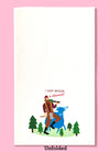 Unfolded dishtowel with the phrase I got wood in Wisconsin in red with an illustration of a cartoon Paul Bunyan and Babe the Blue Ox above tiny trees in a green field