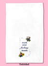 Unfolded dishtowel with the phrase wash your fucking hands. The text is surrounded by illustrations of flowers in the upper right and lower left of the design and dark blue squiggles in the upper left and lower right