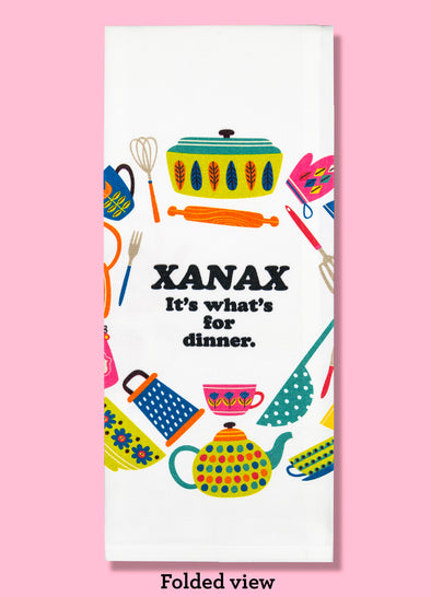Folded dishtowel with the satirical phrase Xanax it's what's for dinner. The text is surrounded by illustrations of kitchen implements in pastel colors.